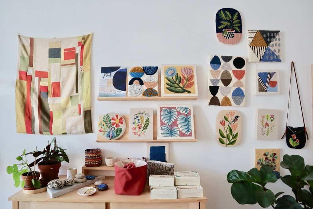 Still life photograph of one wall of Bookou's retail space. On the wall are a series of Arounna's handmade tapestries and woven goods as well as bags and other stationary items.