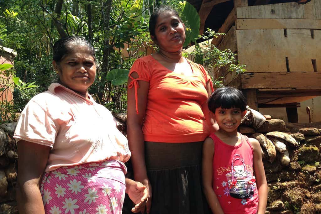 Photograph of two female organic farmers in Sri Lanka standing with a young girl between 7 and 9 years old.