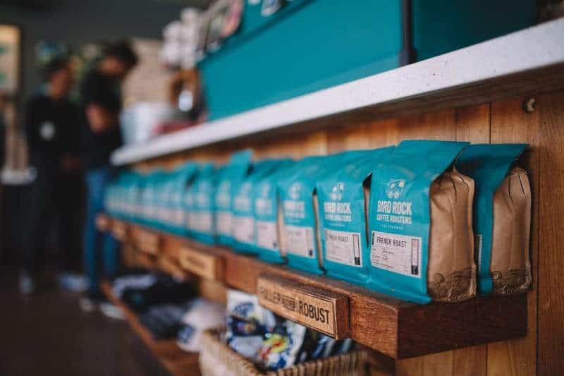 A wooden shelf is lined with several blue bags containing coffee beans