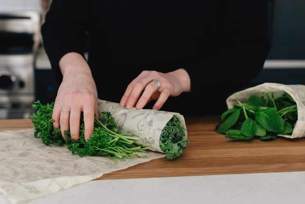 Abeego beeswax wrap being wrapped around parsley and kale.