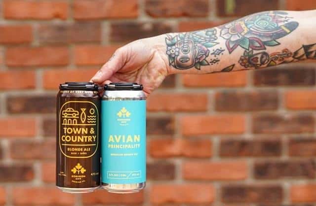 An outstretched tattooed arm and hand holding two cans of beer