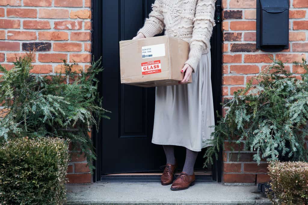 A woman holds a cardboard box on the front step of a brick house