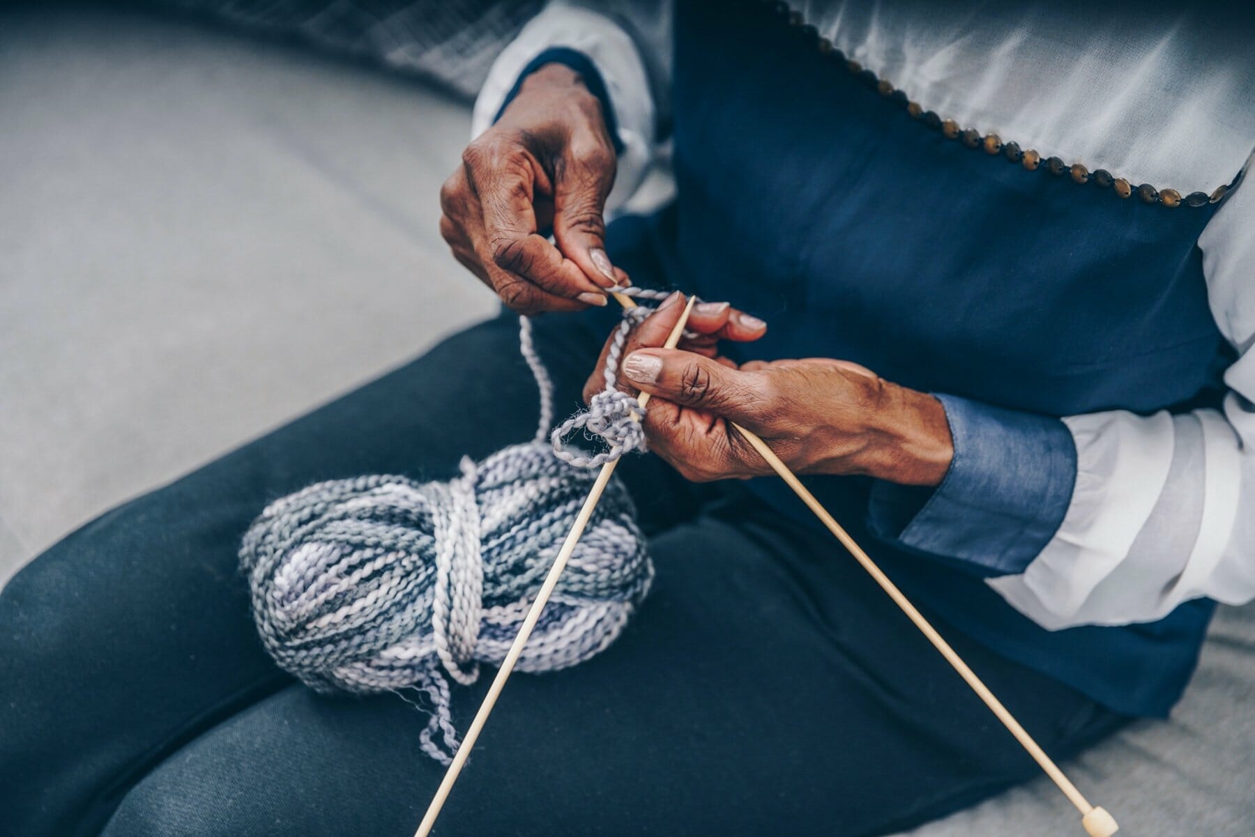 A woman's hands, knitting with grey wool yarn