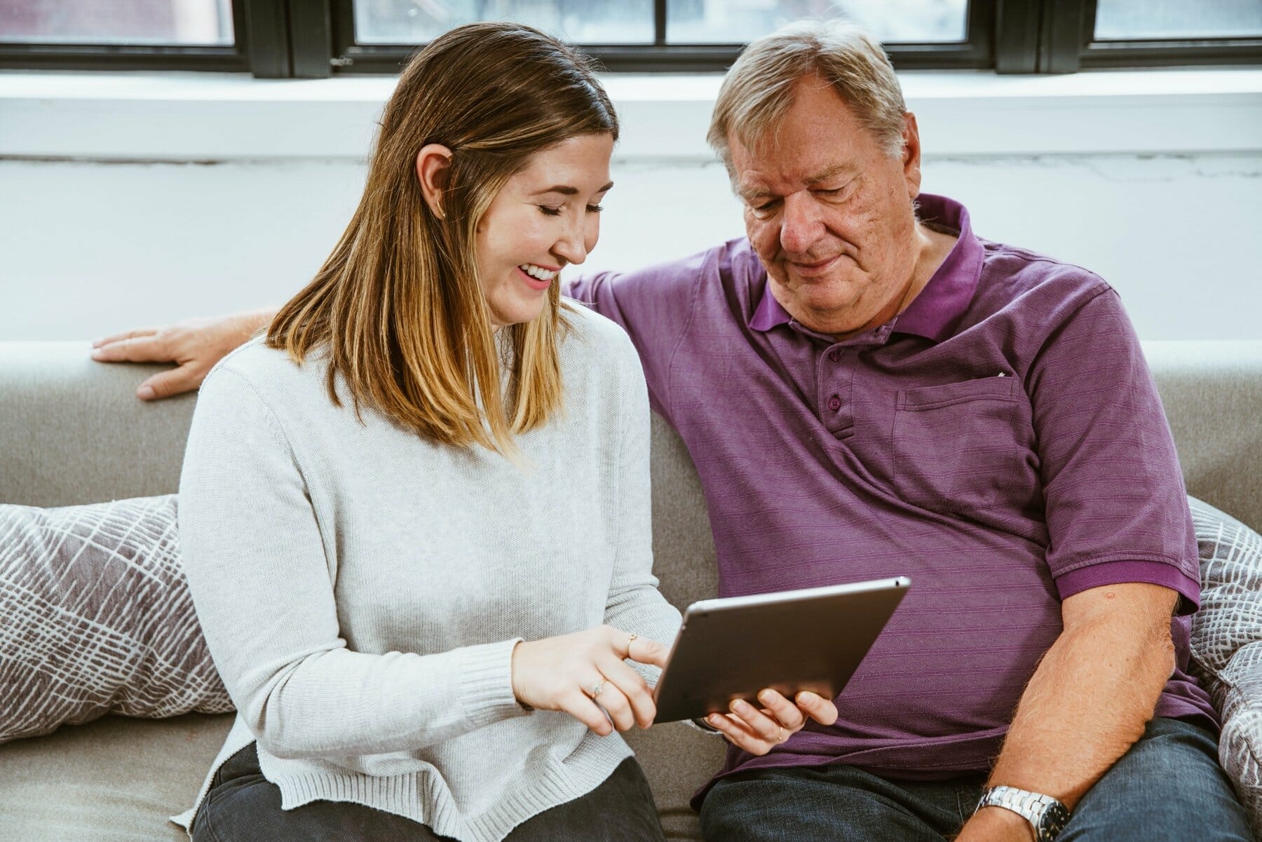 A young woman helps an older man with an iPad