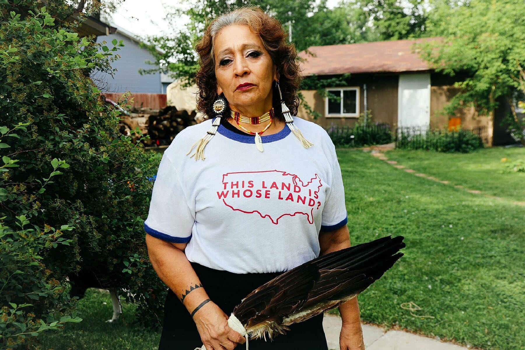 An Indigenous woman stands in a yard wearing a shirt that reads, 