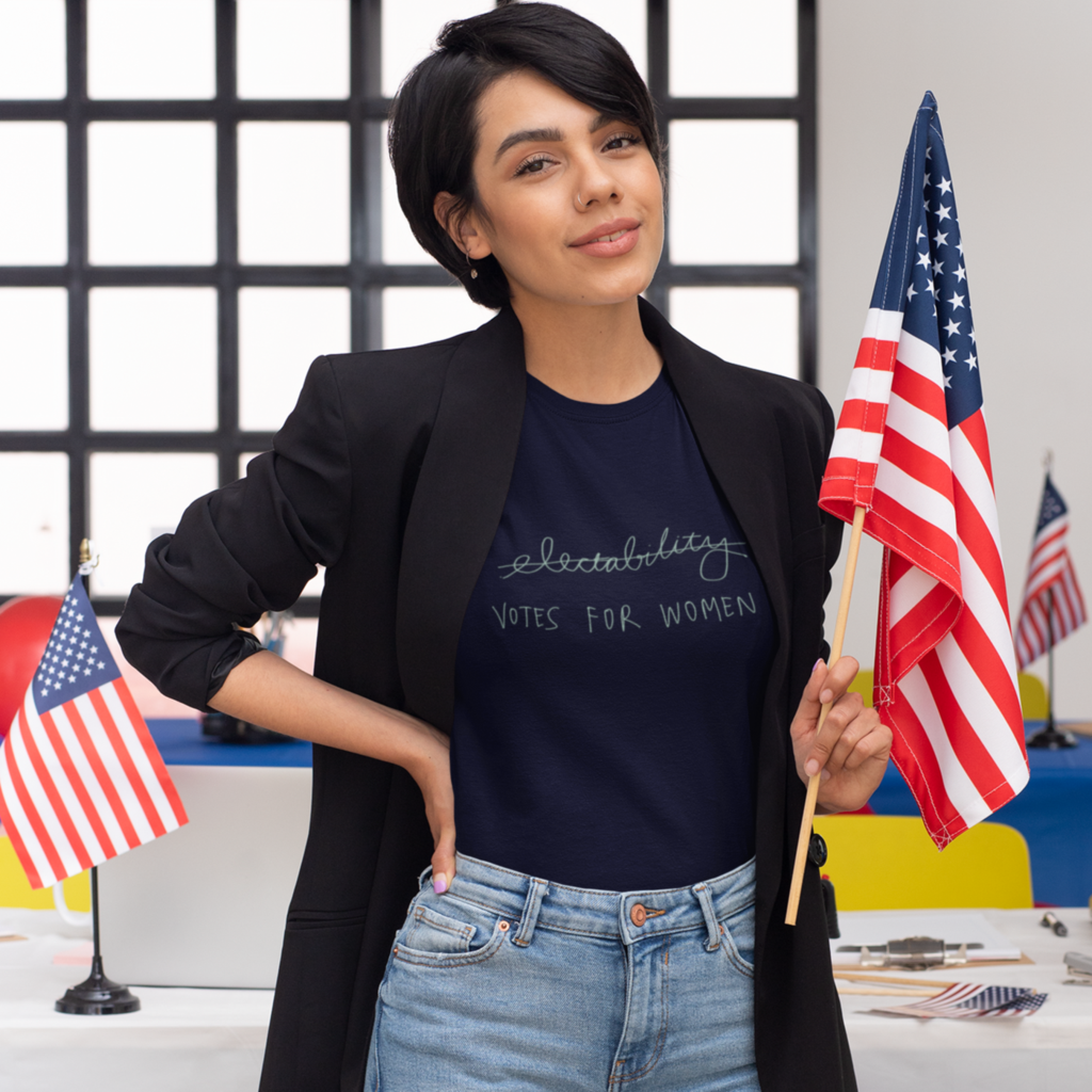 Woman standing in front of a desk with American flags. Her t-shirt reads