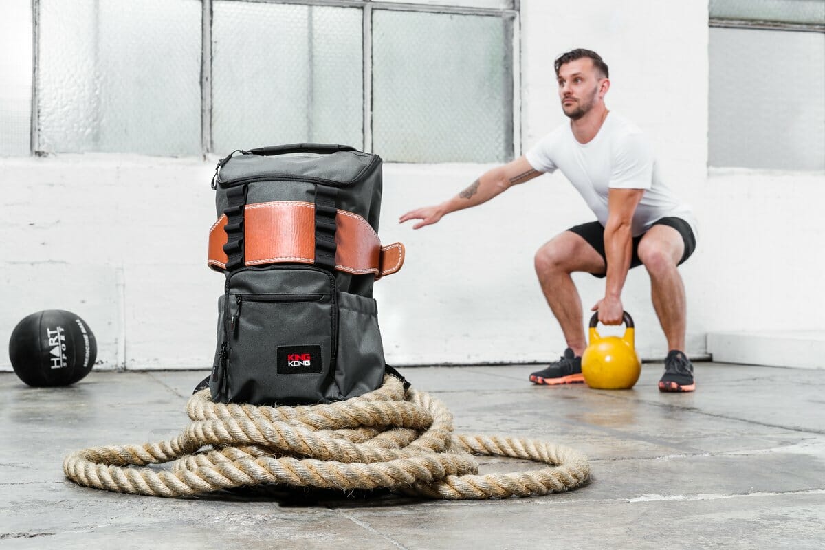 A male model with a kettlebell backdropping a backpack made by King Kong Apparel.