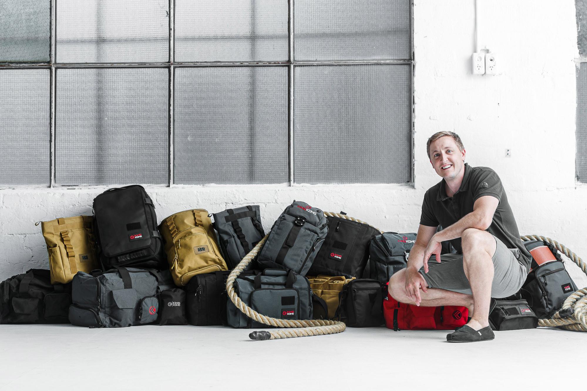 Founder of King Kong Apparel, Stefan Gehrig in a polo shirt and shorts backdropped by various bags made by his brand.