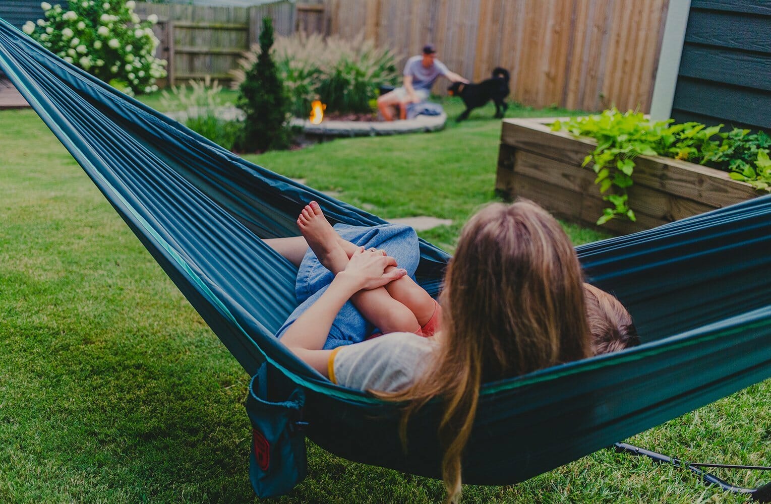 A woman lays in a blue hammock in a grassy yard