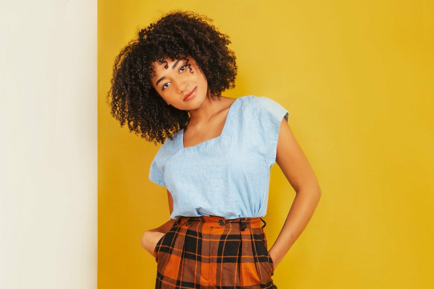 Woman models a blue top and plaid pants against a yellow background