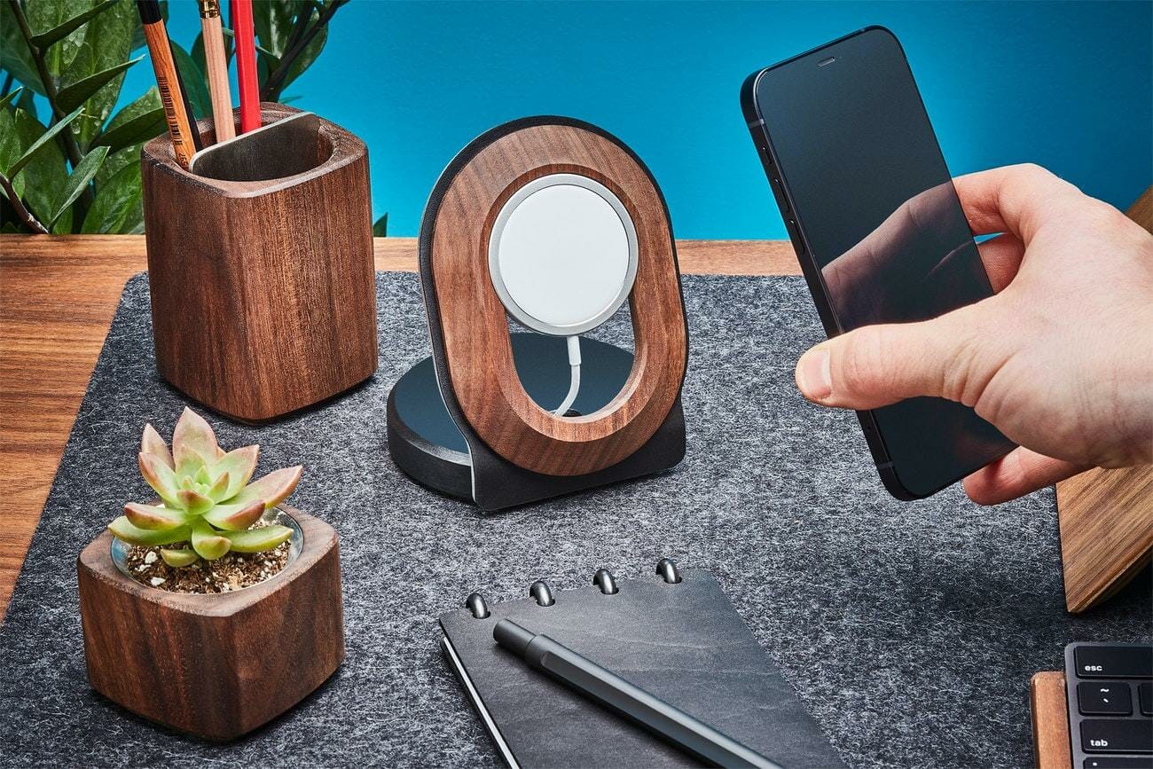 A hand holds a cell phone and wooden and wool office accessories sit on a wooden desk
