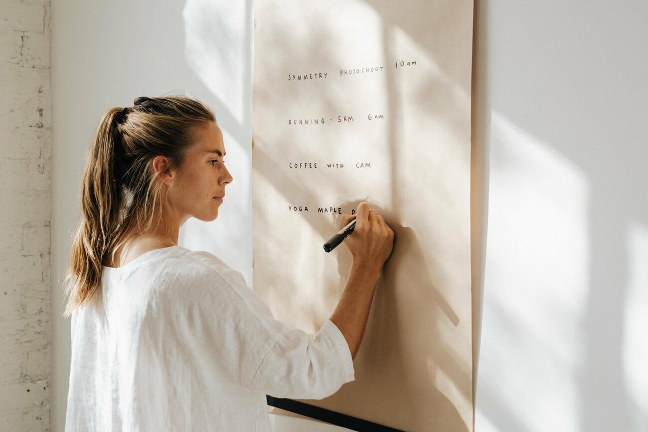 A woman writes on a large paper roller that is affixed to the wall
