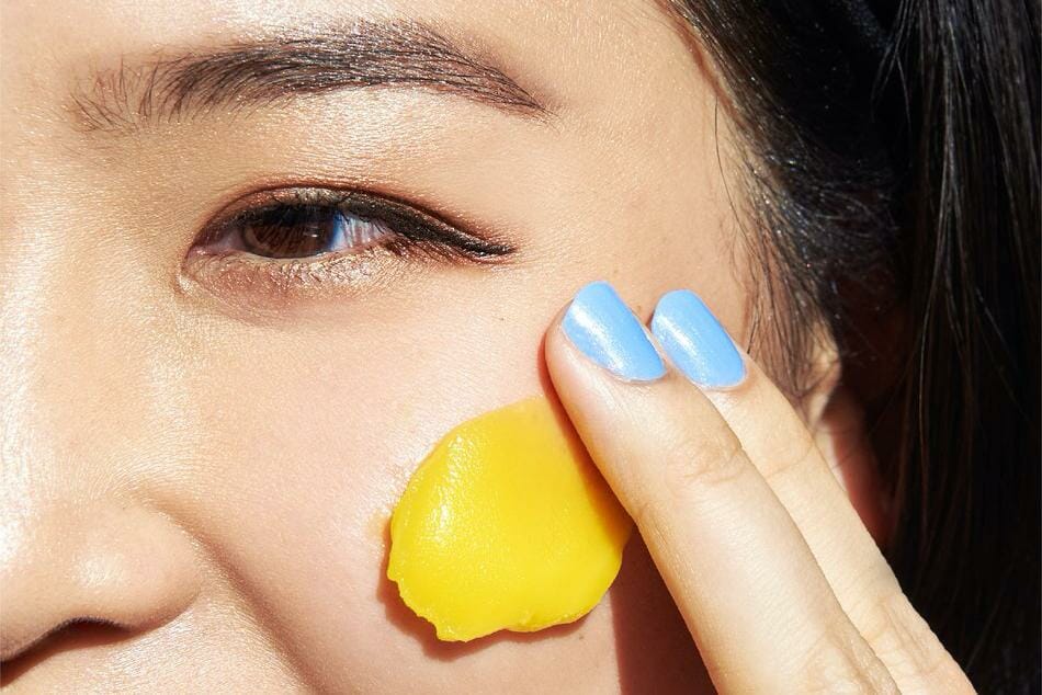A woman rubs a yellow cleanser onto her face
