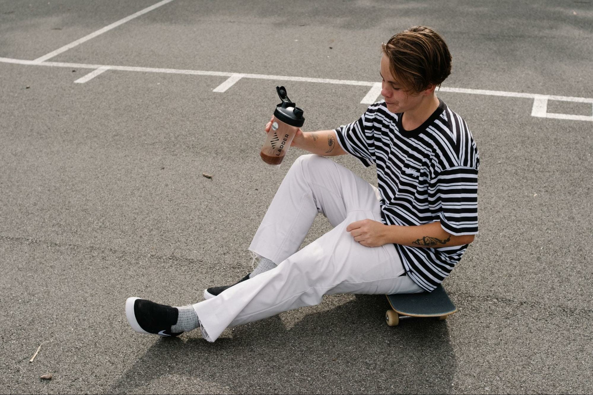 A model sits on a skateboard while drinking Ladder supplements.