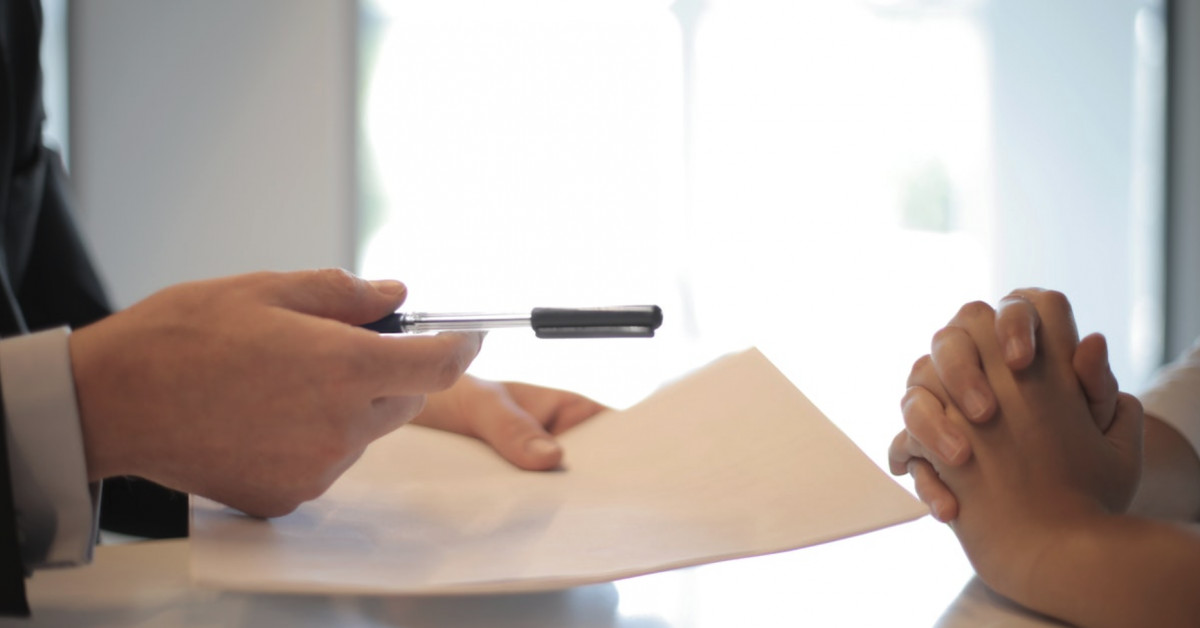 A man in a suit is handing a document to a woman, revealing secrets about General Liability Insurance.
