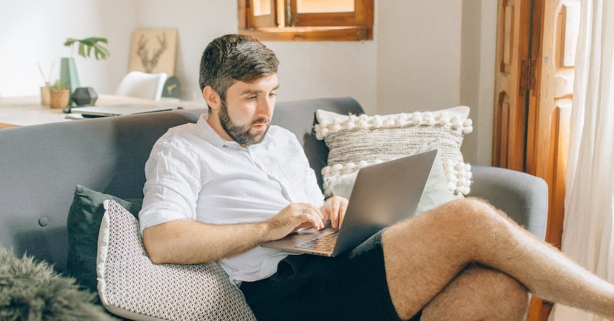 A man sitting on a couch, working on a laptop to achieve business success.