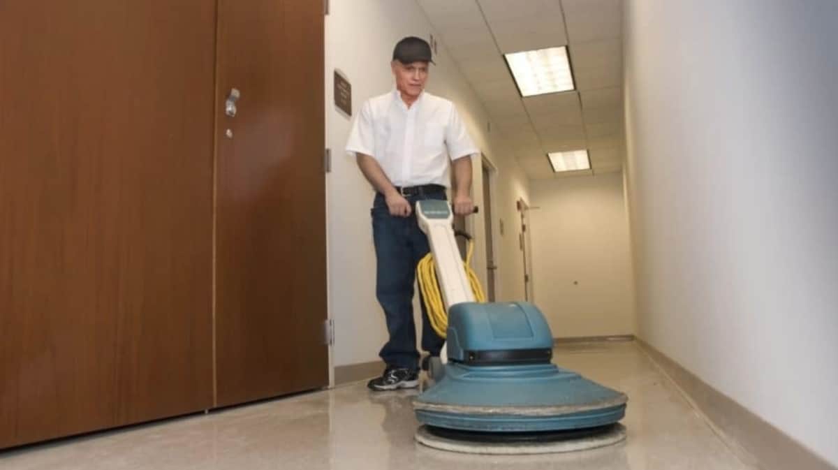 A man cleaning a hallway with a floor polisher in a retail environment.