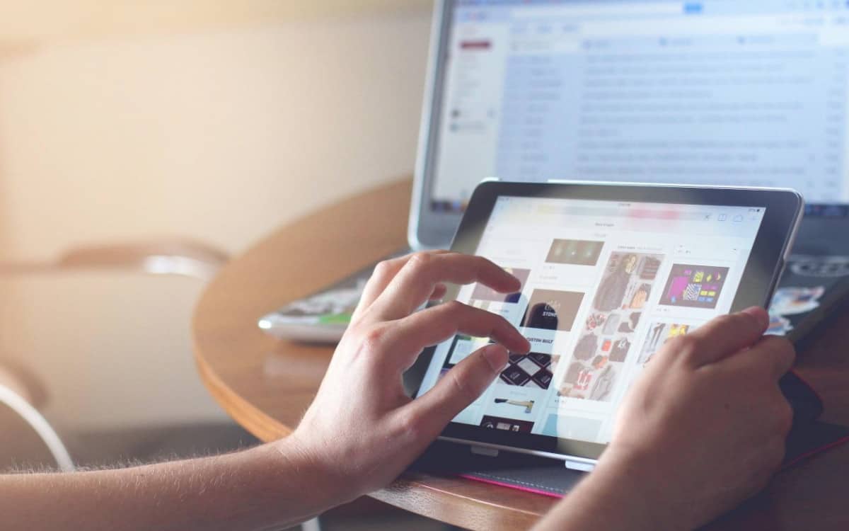 A person multitasking with an iPad and a laptop for academic curricula or online business skills.