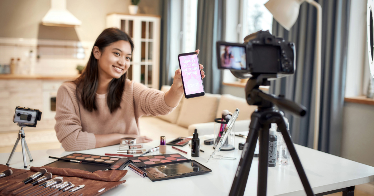 A woman is optimizing her eCommerce business by taking a picture of her makeup while using a video camera.