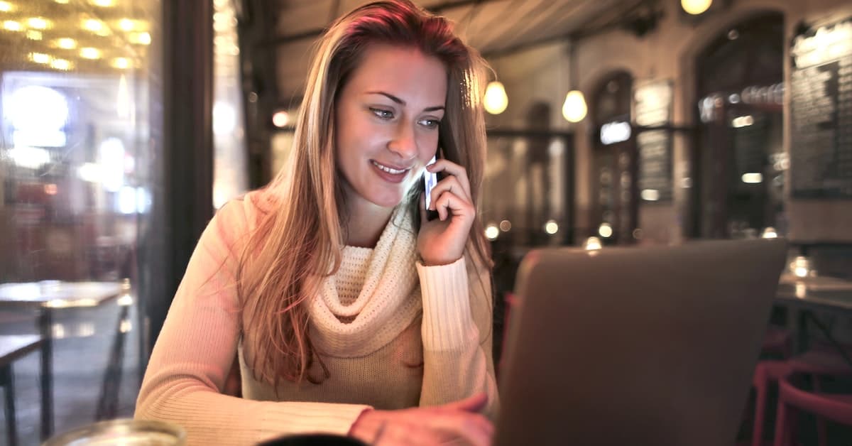 A woman is talking on the phone while sitting at a table in a cafe, building her reputation.