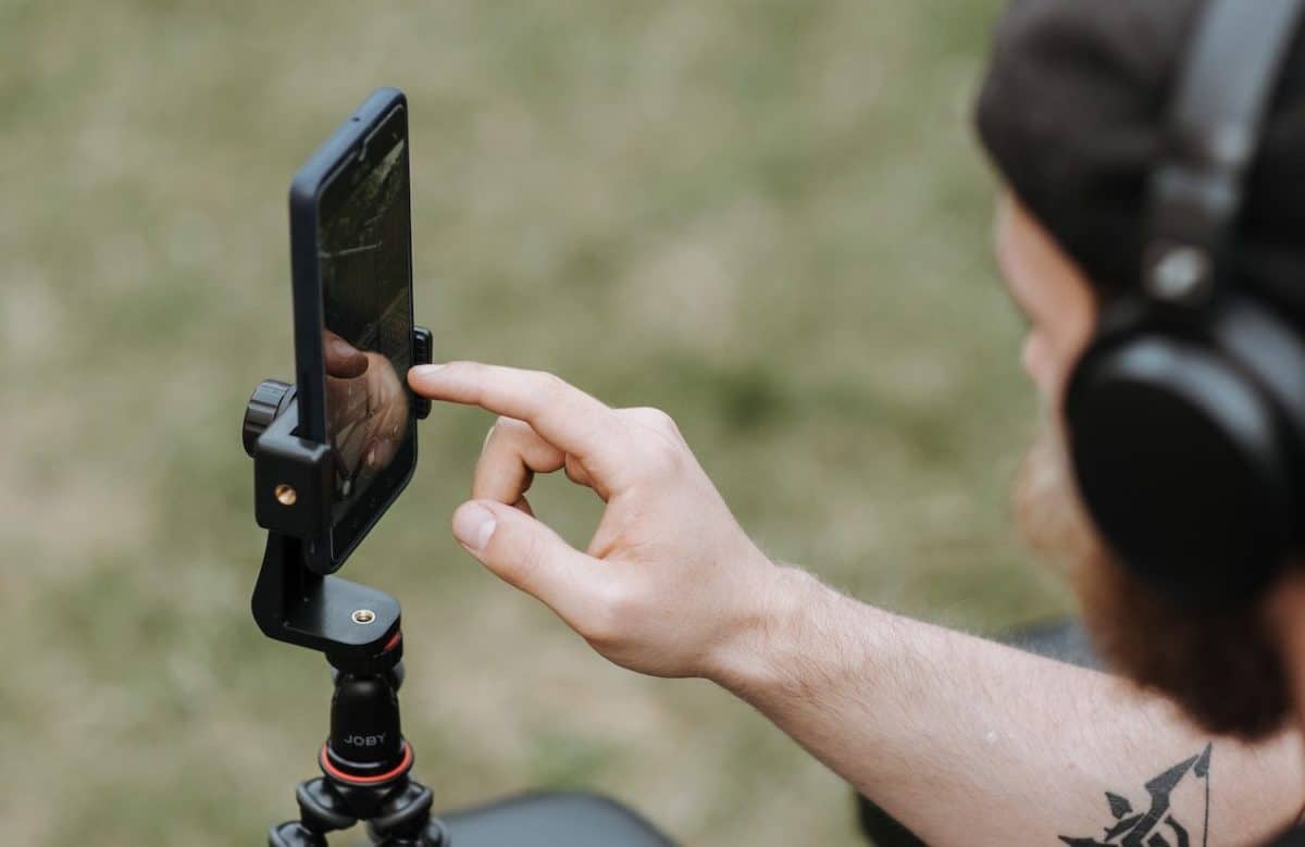 A man with headphones is using a cell phone to take a picture.