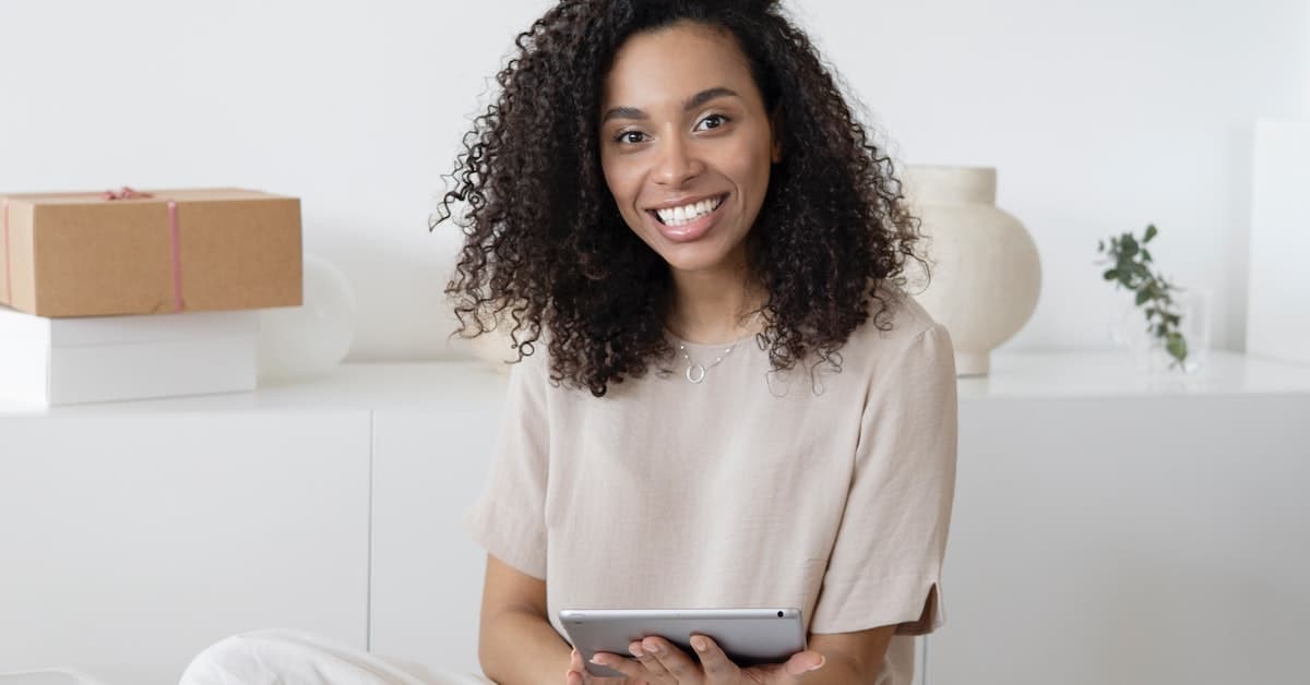 A black woman sitting on the floor with a tablet computer is working on strategies for her small business.
