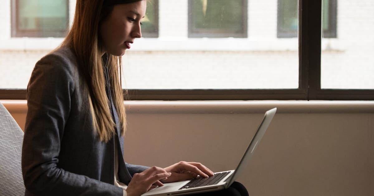 A woman sitting in front of a window, working on her laptop for Ecommerce business sales.