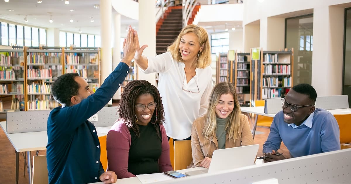 A group of people in a library giving each other high fives during a break from their business meeting.