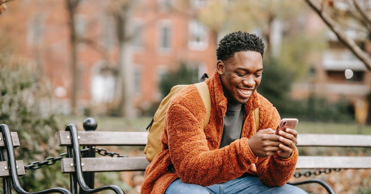 A young man sitting on a bench, engrossed in his phone.