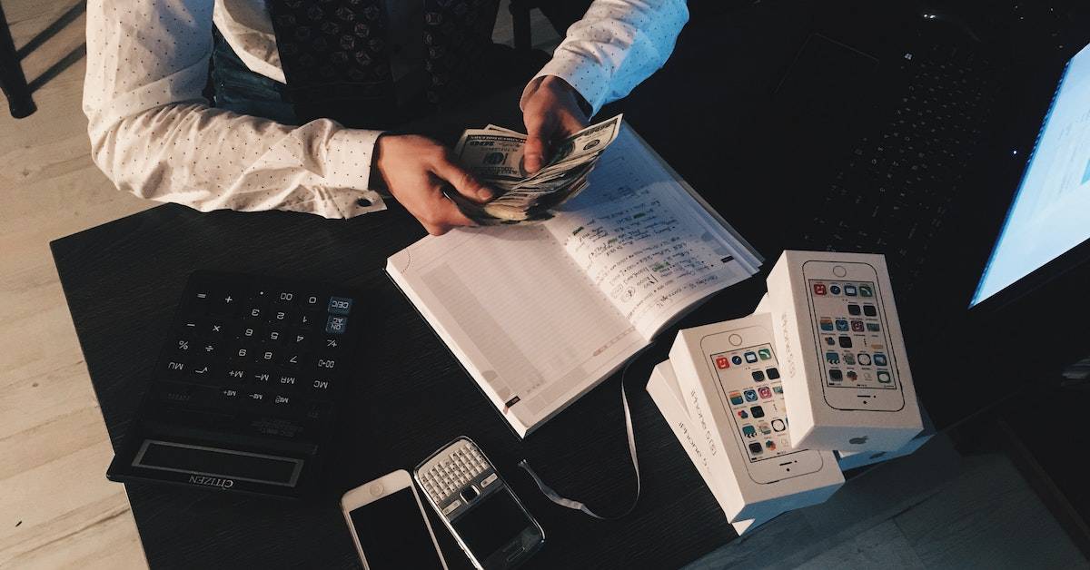 A man is sitting at a desk with money and a calculator, focusing on smart business decisions.