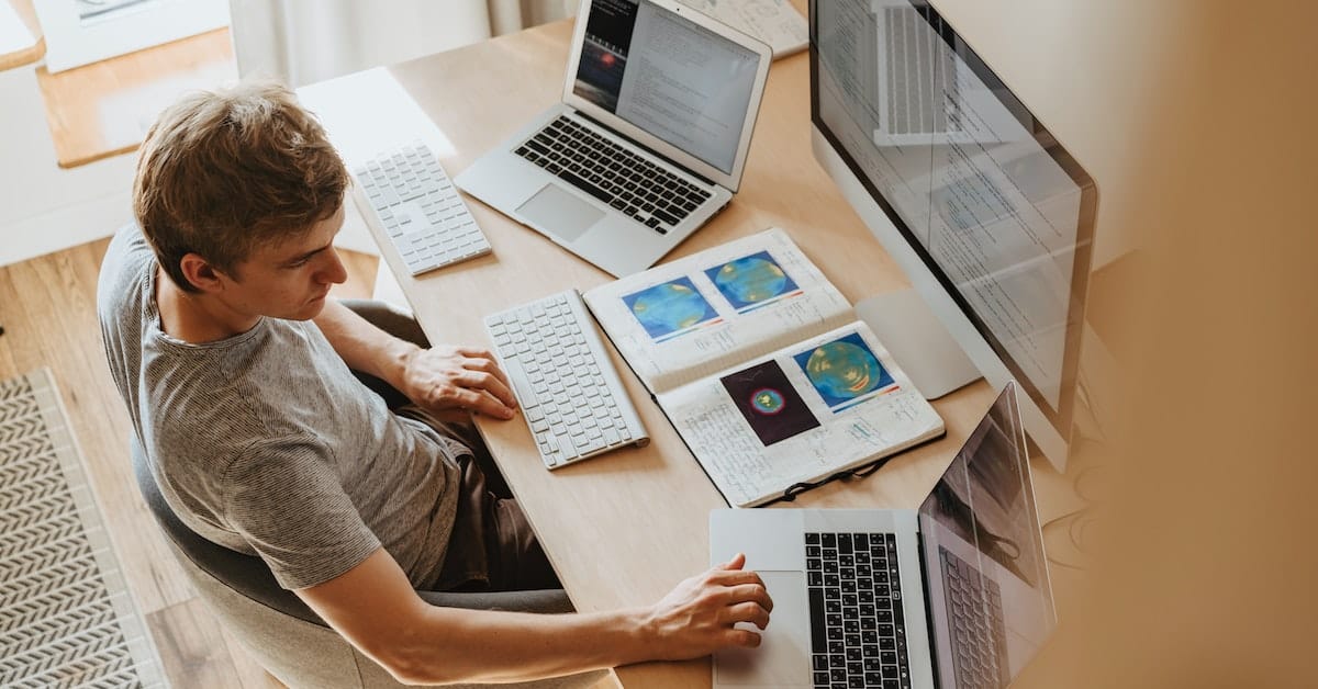 A man sitting at a desk with several laptops, working on an SEO guide for ecommerce.