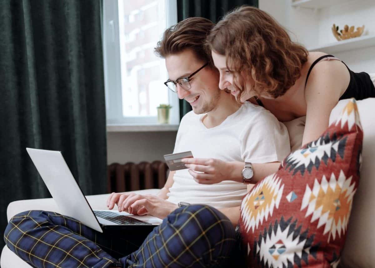 A couple sitting on a couch with a laptop and credit card for online shopping.