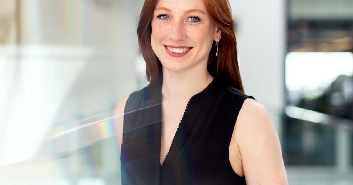 A woman with red hair smiling in an office while balancing work.