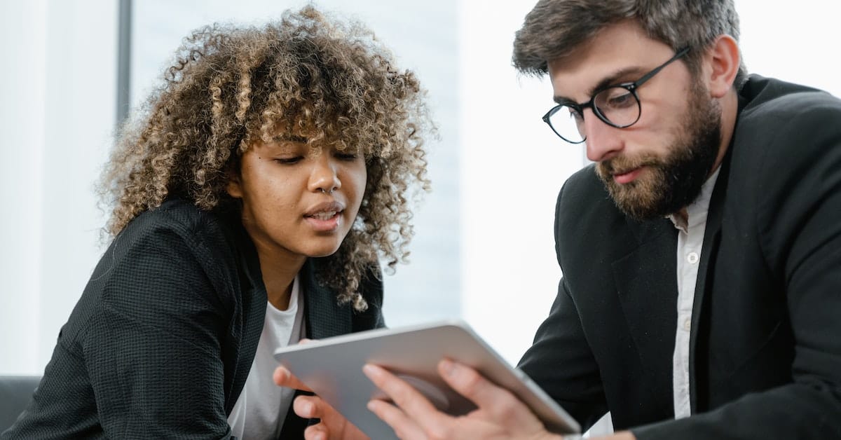 Two business people revolutionizing their pricing strategy by looking at a tablet in an office.