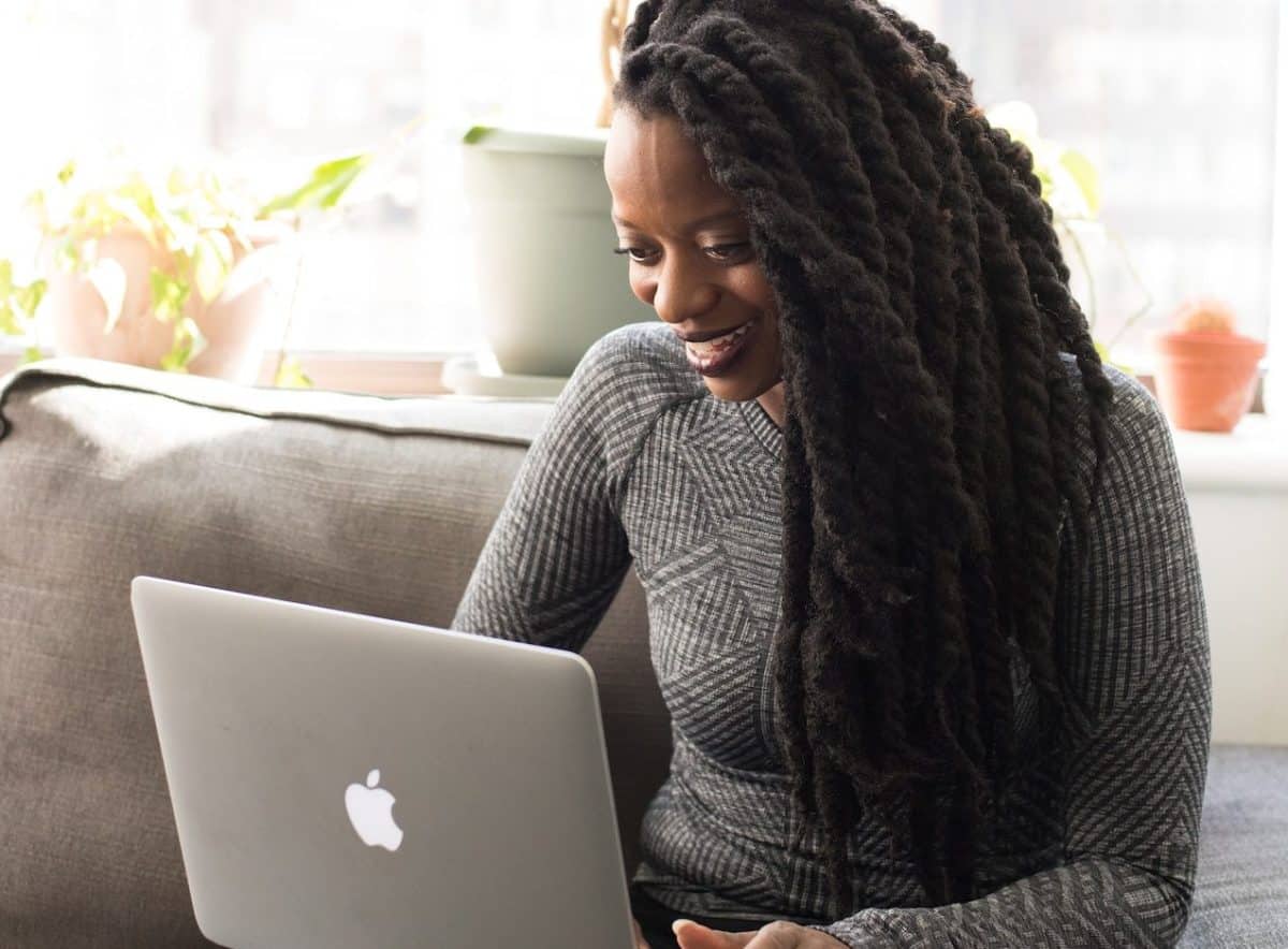A woman with dreadlocks sitting on a couch using a laptop, working on content optimization.