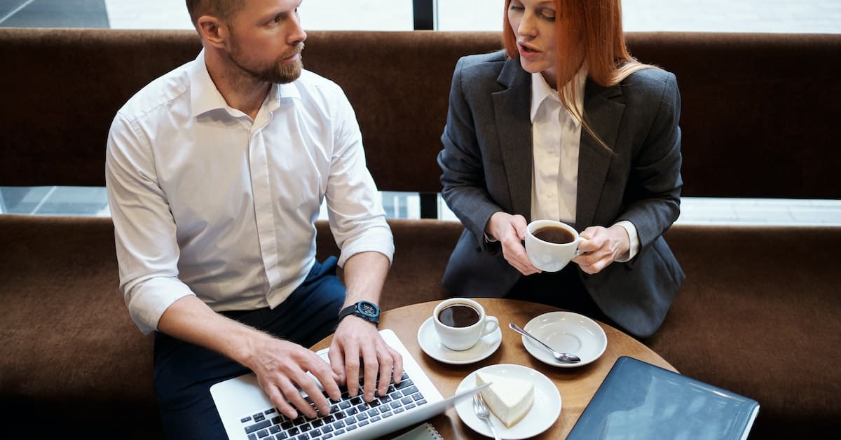 A man and woman are sitting at a table, creating business content on a laptop.