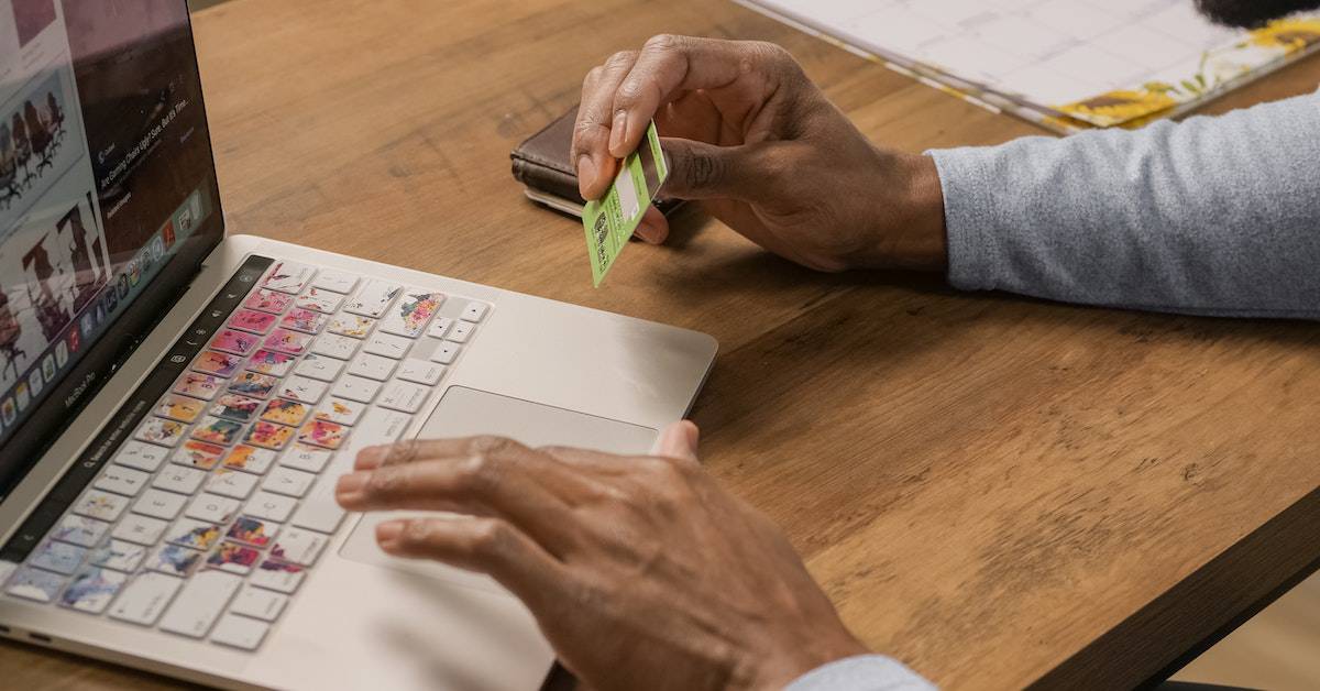 A man holding a credit card while browsing a WooCommerce store on his laptop.