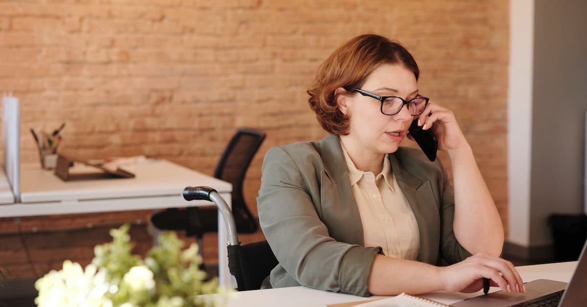 A woman in glasses is talking on the phone while sitting at a desk in the insurance industry.