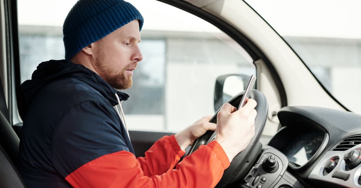 A man sitting in the driver's seat of a car while using his cell phone for last-mile delivery.