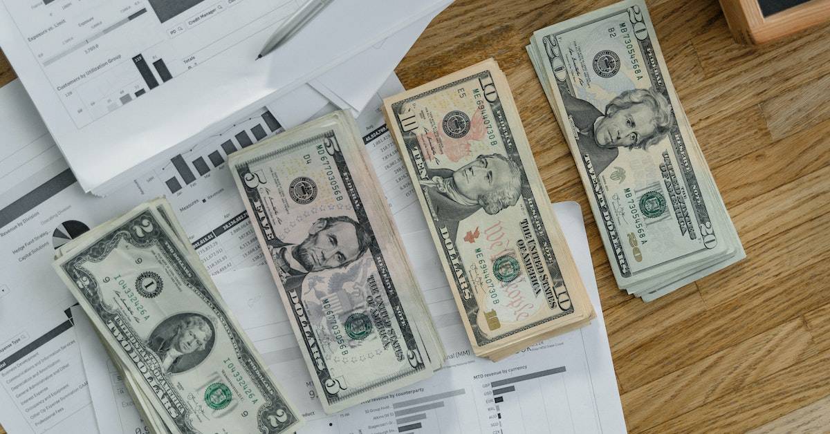 A stack of dollar bills and a calculator sit on a wooden table, used by employers for payroll taxes calculations.