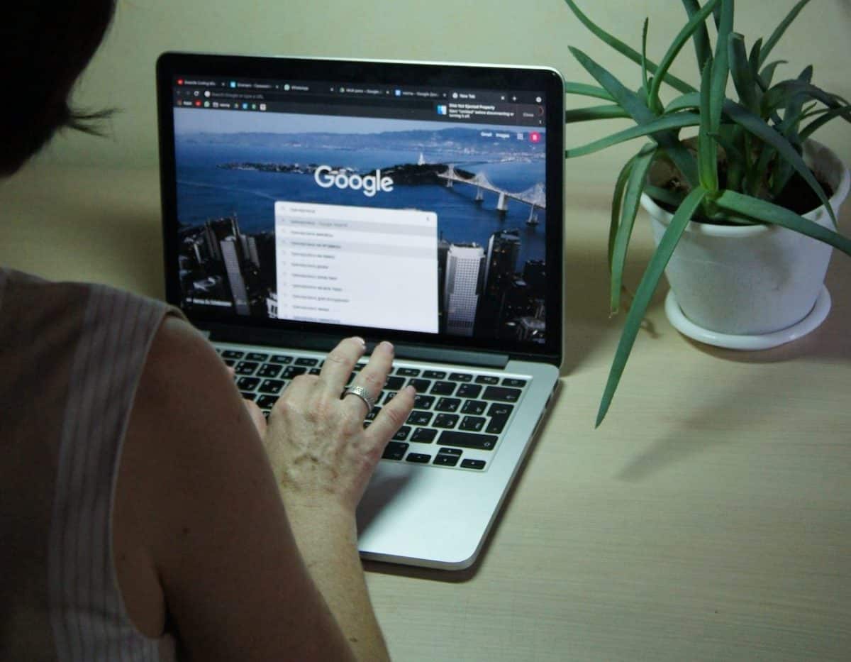 A woman in Glasgow is typing on a laptop with google on the screen.