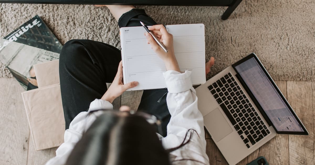 A woman sitting on the floor with a laptop and notebook, implementing strategies.