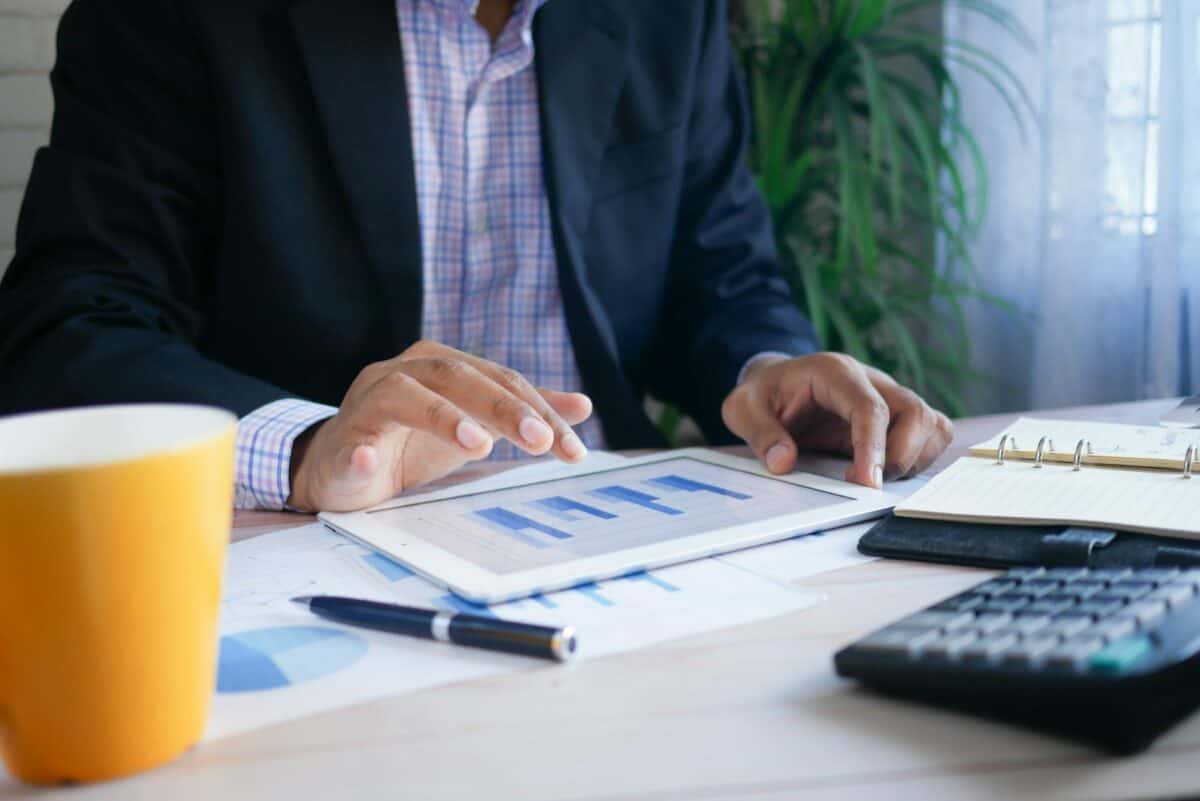 A professional analyzing financial charts on a tablet, with a notepad, pen, and calculator on the desk to enhance their social trading strategy.