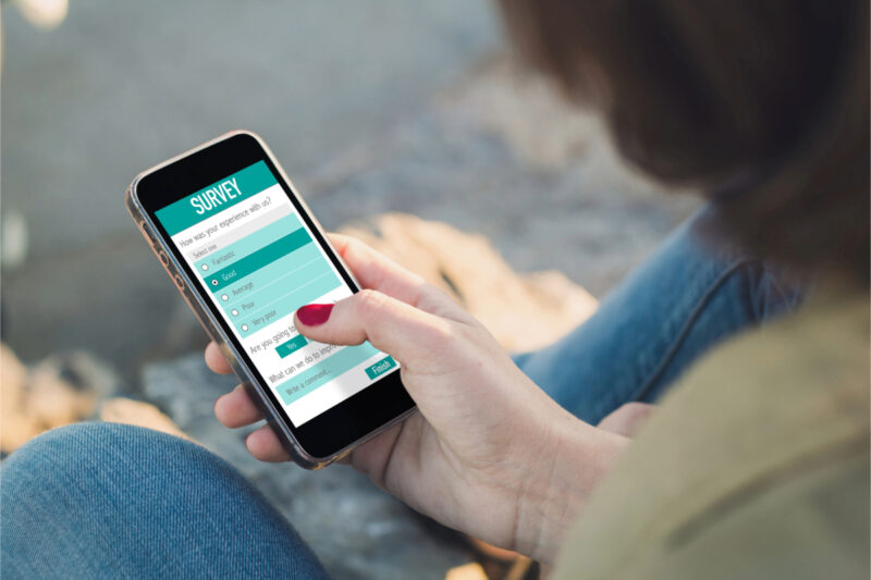 Person holding a smartphone and selecting options on a customer satisfaction survey displayed on the screen.