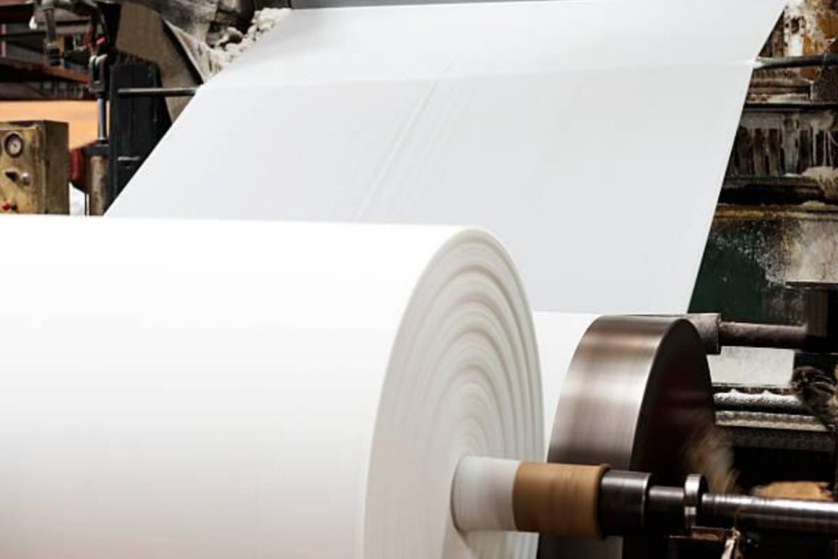 Large roll of paper being processed in industrial printing press machinery for a lucrative career in paper engineering.
