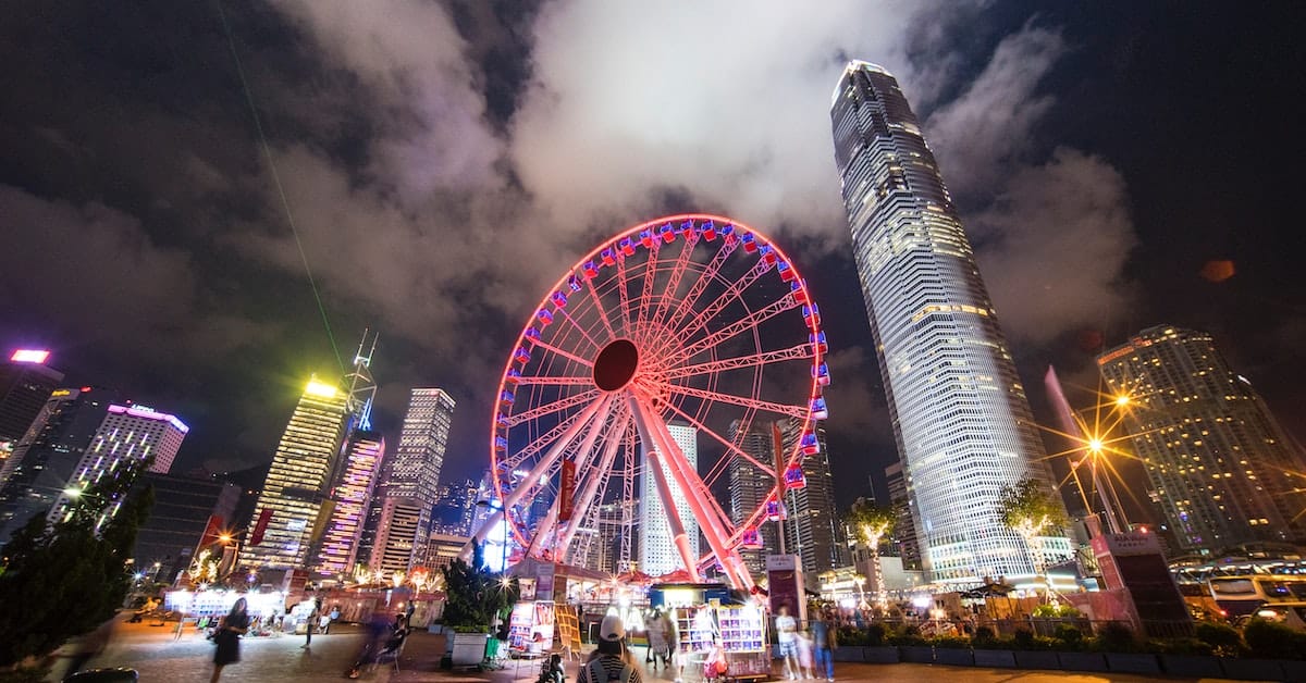 Nighttime cityscape featuring a brightly lit ferris wheel and a skyscraper under a cloudy sky, with people visible in the foreground discussing E-Commerce Opportunities.