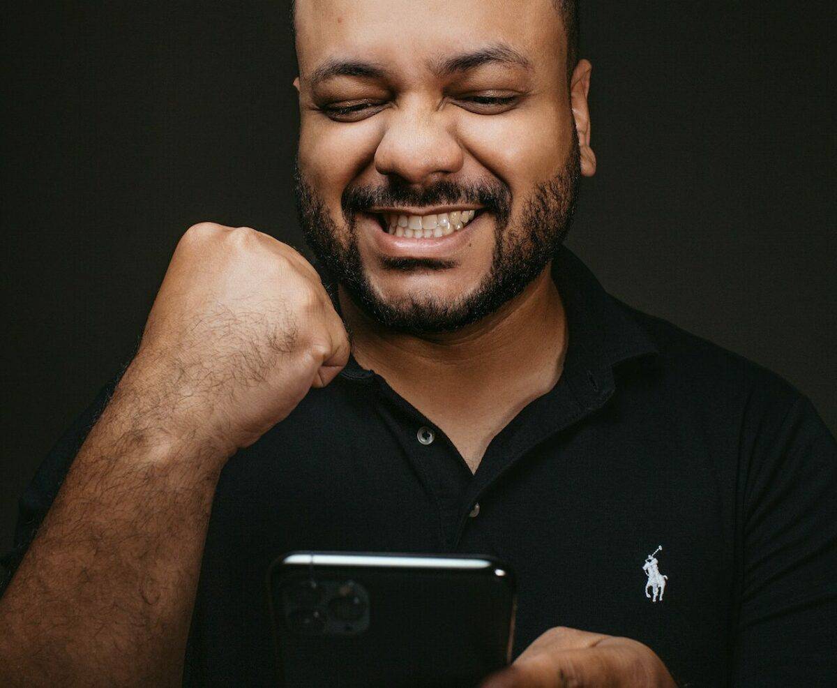 Man smiling while looking at his smartphone, punching the air with his fist in a celebratory gesture after achieving eCommerce business success, against a dark background.
