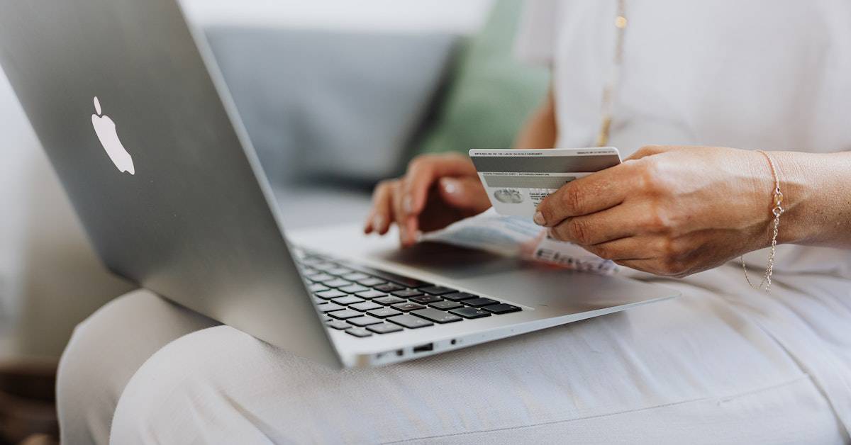 A person holding a credit card while using a laptop, focusing on the keyboard and screen of their ecommerce website, with a visible apple logo.