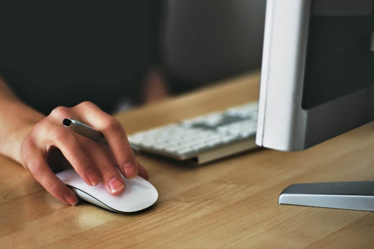 A woman is utilizing a computer mouse on a wooden desk to drive site conversion and boost customer satisfaction in e-commerce.