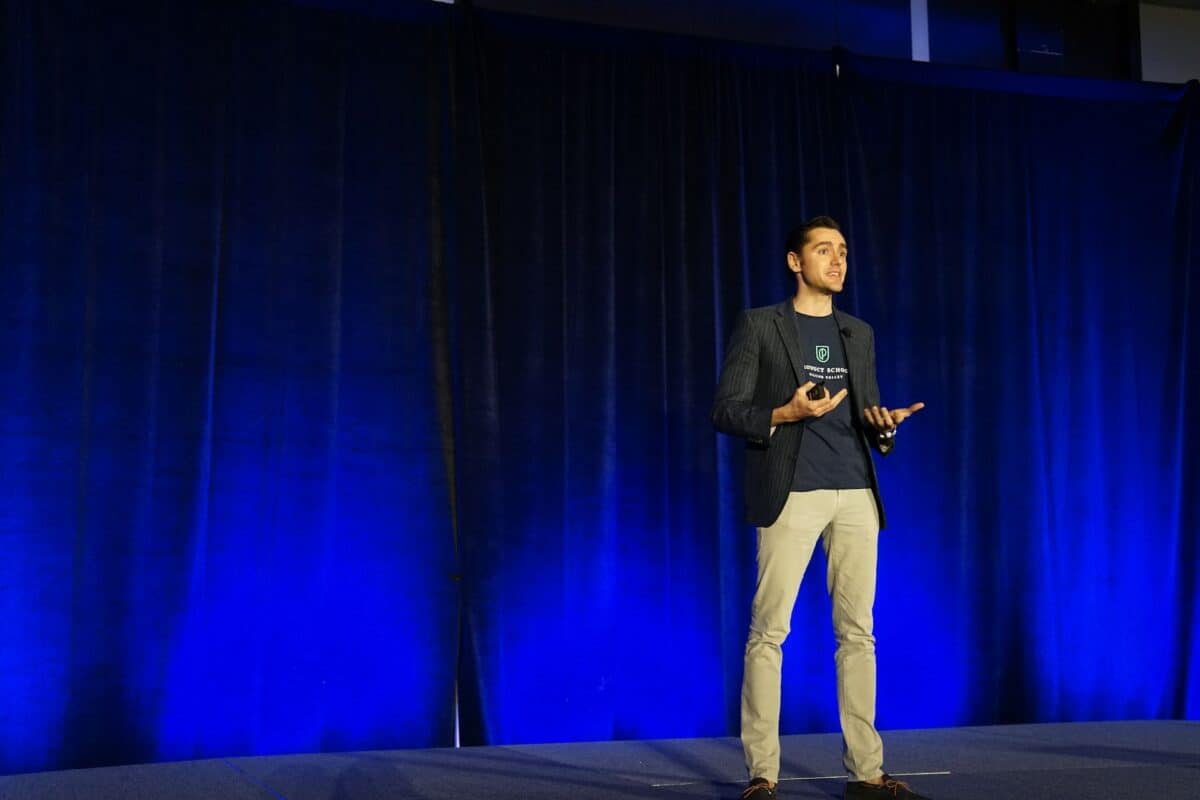 A man expertly presenting on stage with a blue curtain backdrop.